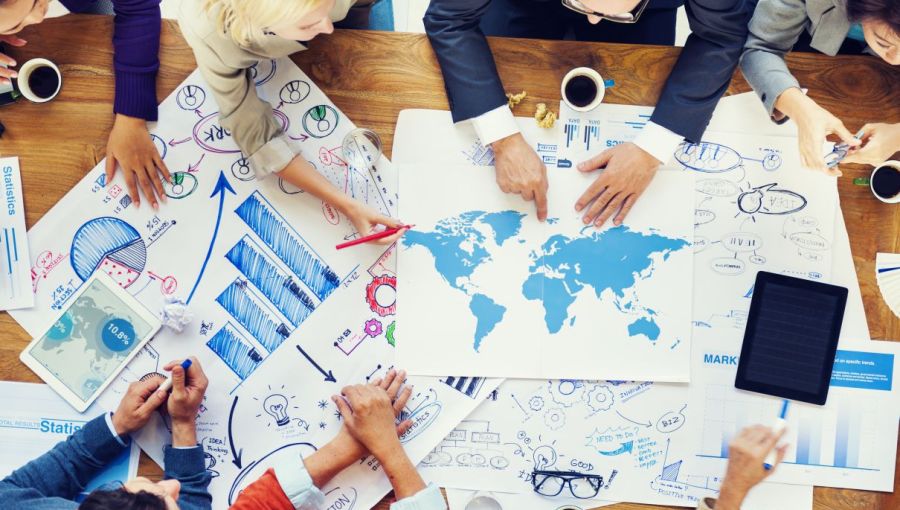 Internationales Business-Team analysiert Weltkarte und Diagramme als Grundlage für Übersetzung und Lokalisierung von Unternehmensinhalten.